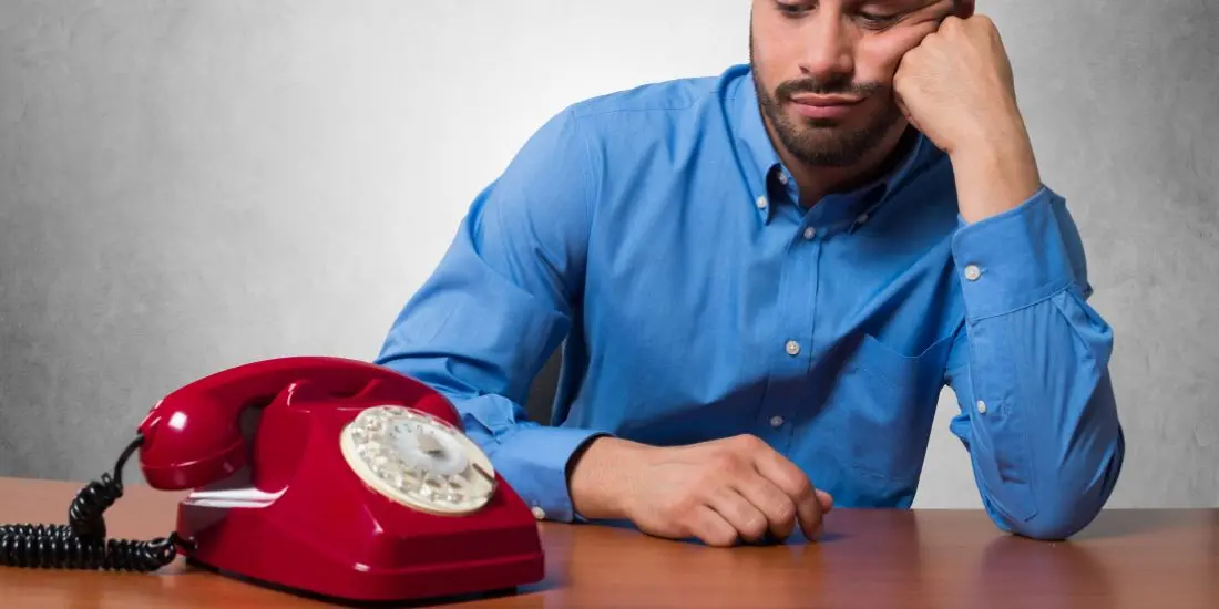 Gefrustreerde professional wachtend op een belangrijk telefoongesprek, benadrukt de noodzaak van effectieve telefoondiensten aangeboden door Office Angels.
