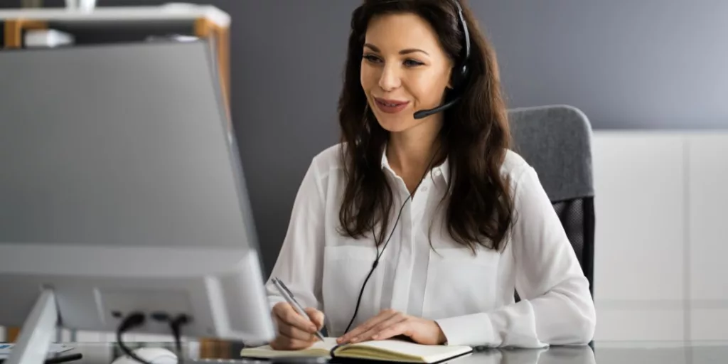Een Virtual Assistant van Office Angels met headset beantwoordt vragen en noteert klantinformatie, het toonbeeld van professionele ondersteuning.