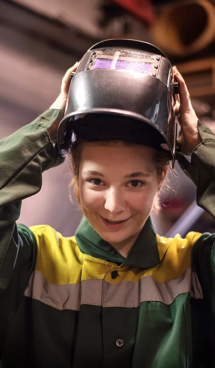 Vrolijke jonge vakvrouw zet veiligheidshelm op in werkplaats, klaar voor technisch project