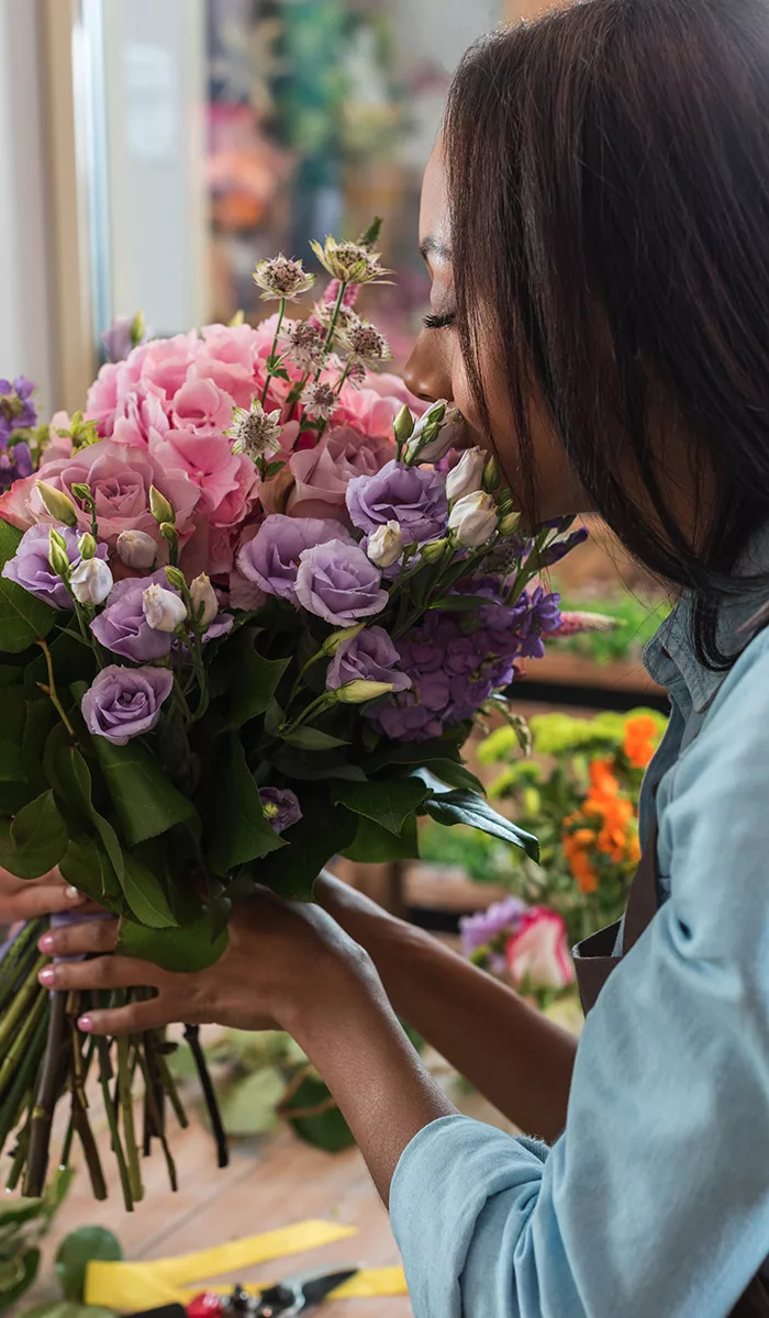 Bloemiste ruikt aan vers boeket, omringd door kleurrijke bloemen, kwaliteitsvakmanschap